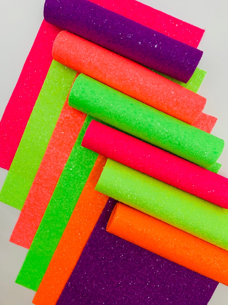 Pu&ograve; includere: Una collezione di rotoli di tessuto glitterato verde neon, arancione e rosa. I rotoli sono impilati uno sopra l'altro, con i rotoli verdi in basso e i rotoli rosa in alto.
