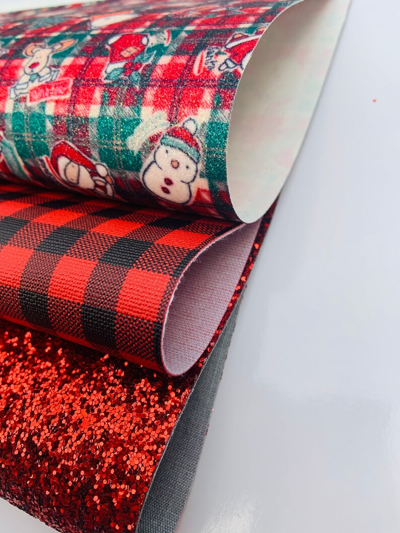 May include: Three red and black patterned fabric sheets. The top sheet features a red and green plaid pattern with a white background and a repeating pattern of Christmas characters. The middle sheet is a red and black buffalo plaid pattern. The bottom sheet is a red glitter fabric.