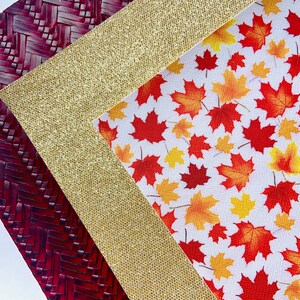 May include: A close-up of three fabric swatches. The top swatch is a red woven fabric with a herringbone pattern. The middle swatch is a gold glitter fabric. The bottom swatch is a white fabric with a red and orange maple leaf pattern.