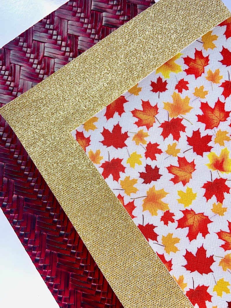 May include: A close-up of three fabric swatches. The top swatch is a red woven fabric with a herringbone pattern. The middle swatch is a gold glitter fabric. The bottom swatch is a white fabric with a red and orange maple leaf pattern.
