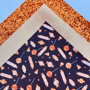 May include: A close-up of three fabric sheets. The top sheet is a sparkly copper color, the middle sheet is a light beige, and the bottom sheet is black with a repeating pattern of orange and white candy.