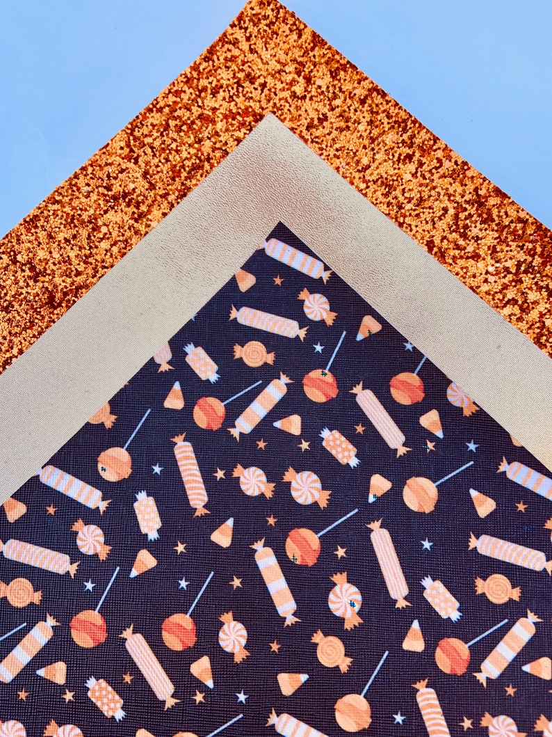 May include: A close-up of three fabric sheets. The top sheet is a sparkly copper color, the middle sheet is a light beige, and the bottom sheet is black with a repeating pattern of orange and white candy.