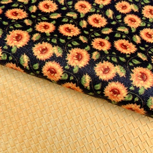 May include: A black fabric with a repeating pattern of orange sunflowers. The fabric is folded over a yellow textured fabric.