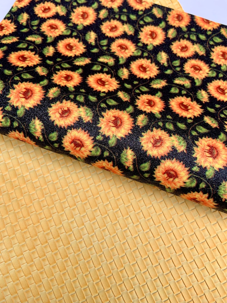 May include: A black fabric with a repeating pattern of orange sunflowers. The fabric is folded over a yellow textured fabric.