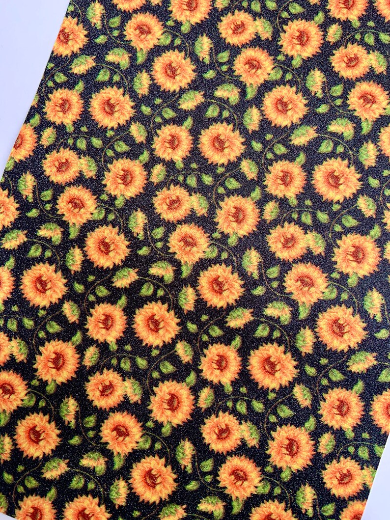 May include: A black fabric with a repeating pattern of yellow sunflowers with green leaves. The fabric has a subtle glitter texture.
