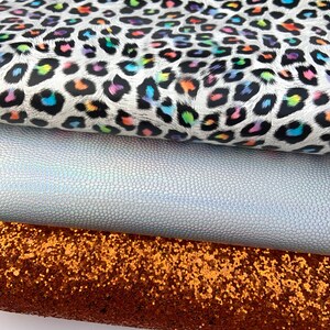 May include: Three fabric swatches: a white fabric with a rainbow leopard print, a silver iridescent fabric with a textured surface, and a copper glitter fabric.