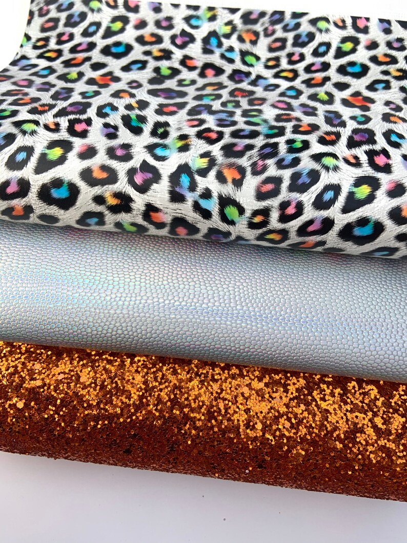 May include: Three fabric swatches: a white fabric with a rainbow leopard print, a silver iridescent fabric with a textured surface, and a copper glitter fabric.