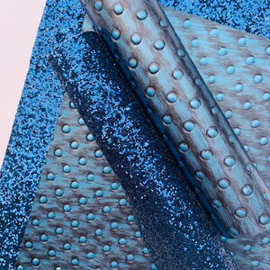 Op de afbeelding: Drie vellen blauw kunstleer met verschillende texturen. Een vel is een effen blauwe glitter, een ander is een blauw en zwart houtnerf met een stippenpatroon, en de derde is een blauw en zwart houtnerf met een groter stippenpatroon.