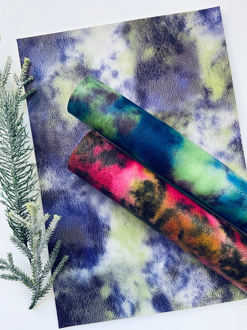 Puede incluir: Dos hojas de piel sint&eacute;tica con un patr&oacute;n de tie-dye. Una hoja es azul, verde y negra. La otra hoja es roja, naranja y negra.
