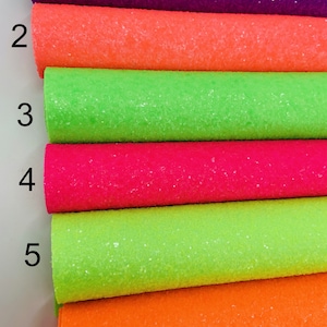 Pu&ograve; includere: Sei rotoli di tessuto glitterato in vari colori, tra cui viola, arancione, verde, rosa, verde lime e arancione. Il tessuto &egrave; disposto in una pila, con i numeri da 1 a 6 scritti sul lato sinistro dell'immagine.