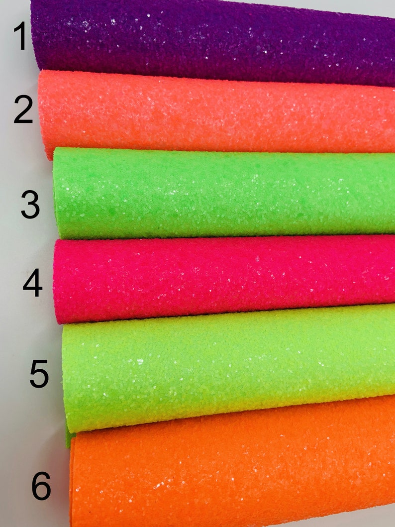 Pu&ograve; includere: Sei rotoli di tessuto glitterato in vari colori, tra cui viola, arancione, verde, rosa, verde lime e arancione. Il tessuto &egrave; disposto in una pila, con i numeri da 1 a 6 scritti sul lato sinistro dell'immagine.