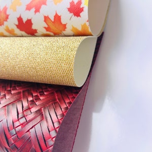 May include: Three different faux leather sheets, one with a red woven pattern, one with a gold glitter pattern, and one with a white background and red and orange maple leaf pattern.