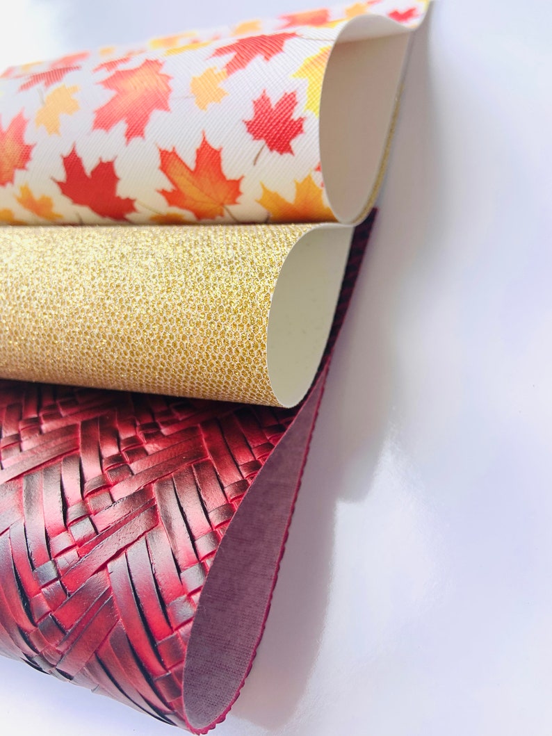 May include: Three different faux leather sheets, one with a red woven pattern, one with a gold glitter pattern, and one with a white background and red and orange maple leaf pattern.