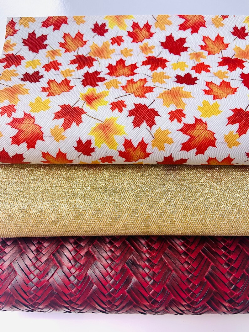 May include: Three pieces of fabric: a white fabric with a red and yellow leaf pattern, a gold glitter fabric, and a dark red woven fabric.