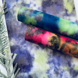 Puede incluir: Dos rollos de piel sint&eacute;tica con un patr&oacute;n tie-dye. Un rollo es azul, verde y negro. El otro rollo es rojo, naranja y negro.