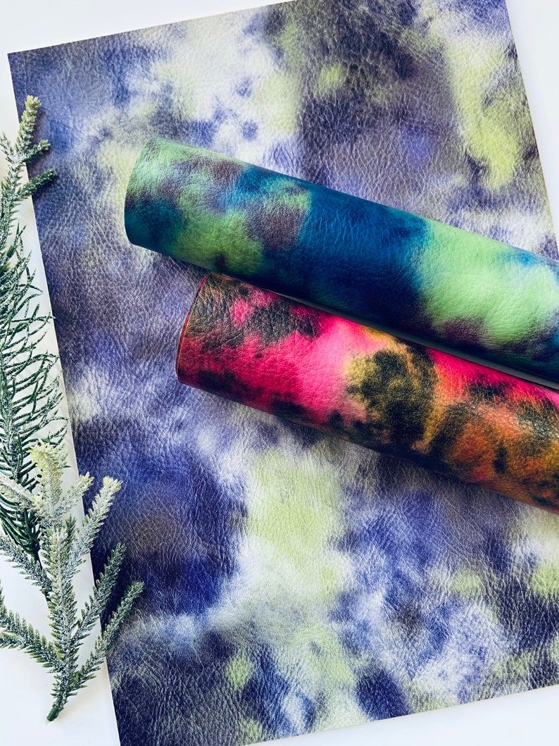 Puede incluir: Dos rollos de piel sint&eacute;tica con un patr&oacute;n tie-dye. Un rollo es azul, verde y negro. El otro rollo es rojo, naranja y negro.