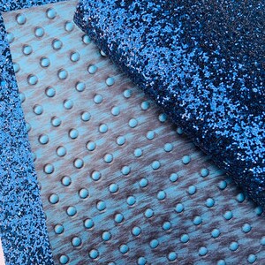 Op de afbeelding: Een close-up van een blauwe glitterstof met een getextureerde blauwe stof eronder. De glitterstof heeft een subtiele glans.