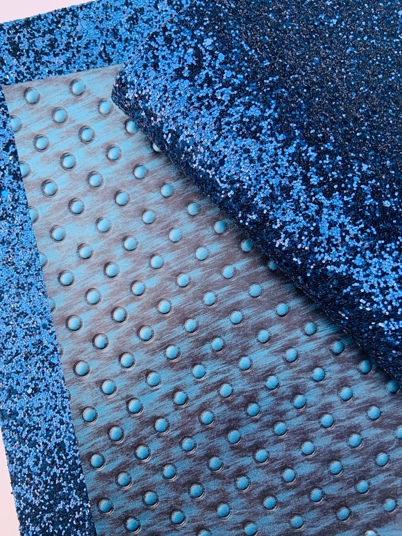 Op de afbeelding: Een close-up van een blauwe glitterstof met een getextureerde blauwe stof eronder. De glitterstof heeft een subtiele glans.