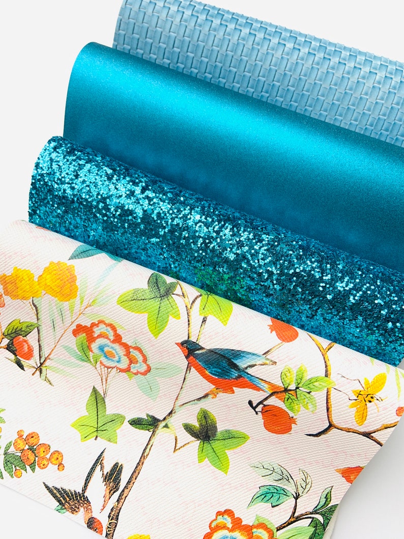 May include: Four different teal coloured fabric swatches. The top swatch is a light blue woven fabric. The second swatch is a solid teal fabric. The third swatch is a teal glitter fabric. The bottom swatch is a white fabric with a floral pattern and birds.
