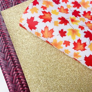 May include: Three sheets of fabric, one with a woven pattern in burgundy, one with a gold glitter finish, and one with a white background and a pattern of red, orange, and yellow maple leaves.