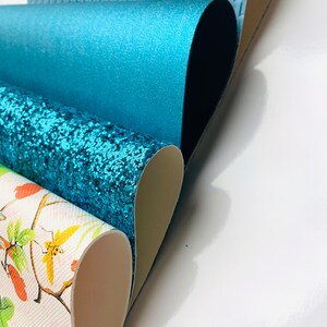 May include: Four different rolls of faux leather fabric in various colours and patterns. The top roll is a light blue woven fabric, the second roll is a solid teal fabric, the third roll is a teal glitter fabric, and the bottom roll is a white fabric with a floral pattern.