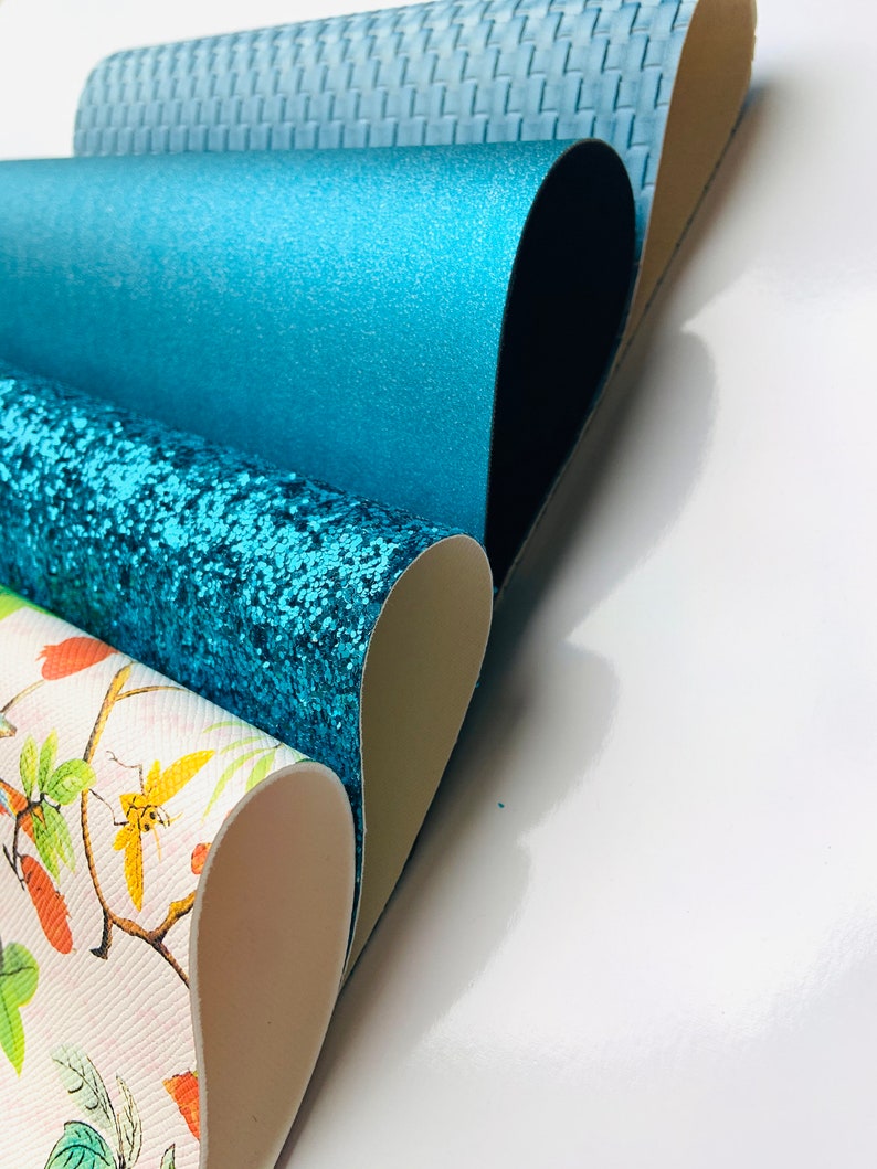 May include: Four different rolls of faux leather fabric in various colours and patterns. The top roll is a light blue woven fabric, the second roll is a solid teal fabric, the third roll is a teal glitter fabric, and the bottom roll is a white fabric with a floral pattern.