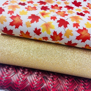 May include: Three pieces of fabric with different textures and patterns. The top piece is white with a red and yellow maple leaf pattern. The middle piece is gold glitter fabric. The bottom piece is a dark red woven fabric.