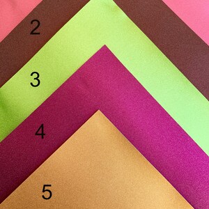 K&ouml;nnte beinhalten: F&uuml;nf unterschiedlich farbige Bl&auml;tter Papier, die in Form eines Dreiecks angeordnet sind. Die Farben sind Koralle, Limettengr&uuml;n, Burgunderrot, Gold und Braun. Die Zahlen 1 bis 5 sind auf der linken Seite jedes Blattes Papier geschrieben.