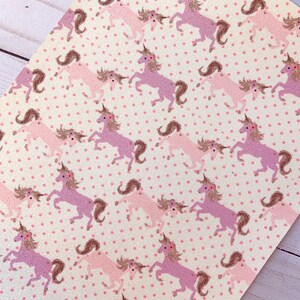 May include: White fabric with a pink and purple unicorn pattern. The unicorns are outlined in brown and have pink flowers on their heads. The background is covered in small pink dots.