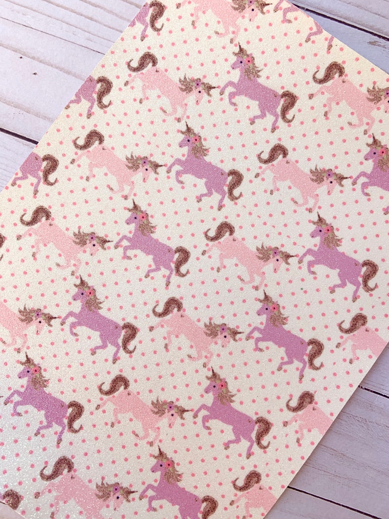 May include: White fabric with a pink and purple unicorn pattern. The unicorns are outlined in brown and have pink flowers on their heads. The background is covered in small pink dots.