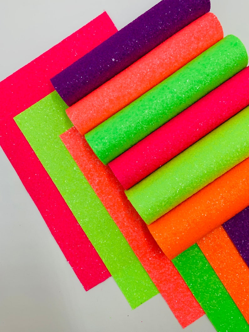 Pu&ograve; includere: Un set di otto fogli di tessuto glitterato in vari colori neon, tra cui rosa, arancione, verde e viola. Il tessuto &egrave; strutturato e ha una finitura scintillante.
