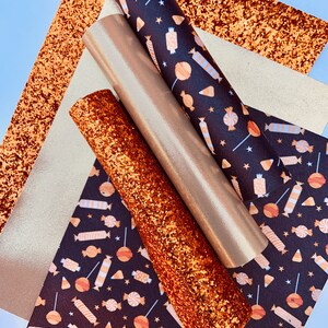 May include: A set of four craft supplies featuring a black and orange candy corn and lollipop pattern, a gold glitter sheet, and two rolls of gold glitter fabric.