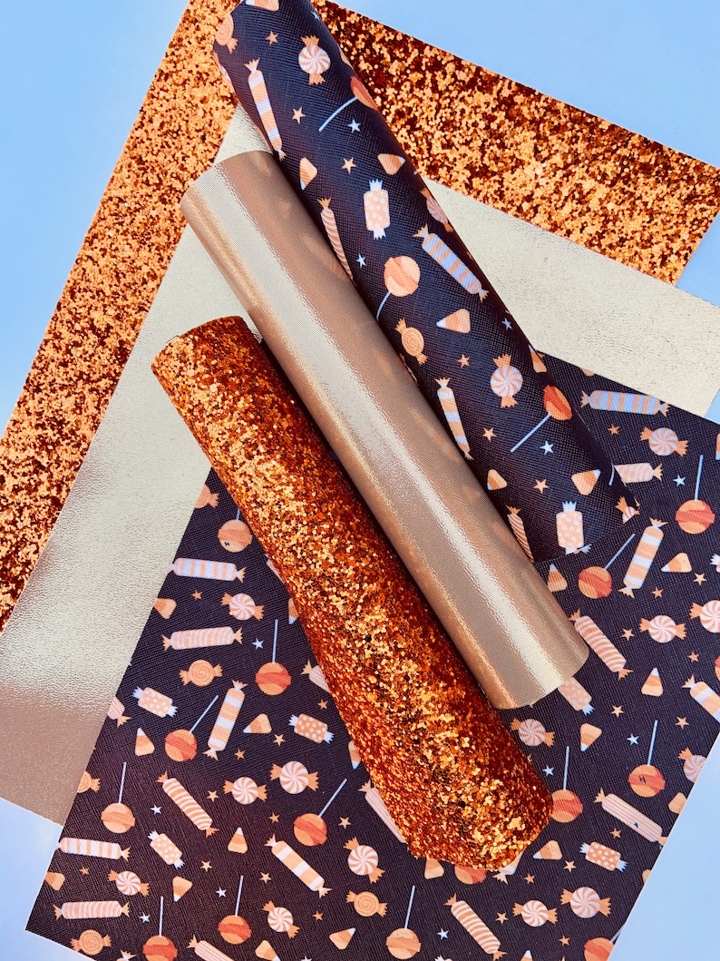 May include: A set of four craft supplies featuring a black and orange candy corn and lollipop pattern, a gold glitter sheet, and two rolls of gold glitter fabric.