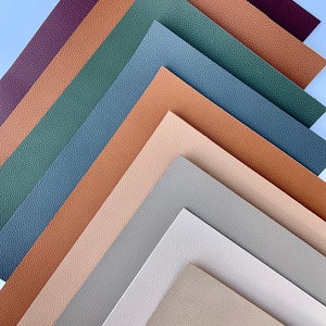 May include: A collection of ten faux leather sheets in various neutral colors, including beige, brown, gray, and green. The sheets are arranged in a staggered pattern, with the top sheet being a deep burgundy color.