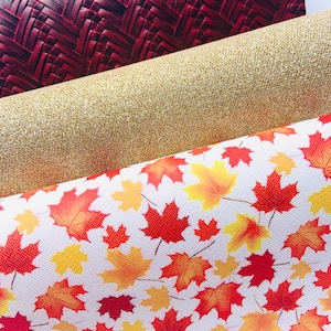 May include: Three fabric swatches with different patterns. The top swatch is a dark red woven fabric. The middle swatch is a gold glitter fabric. The bottom swatch is a white fabric with a red and yellow maple leaf pattern.