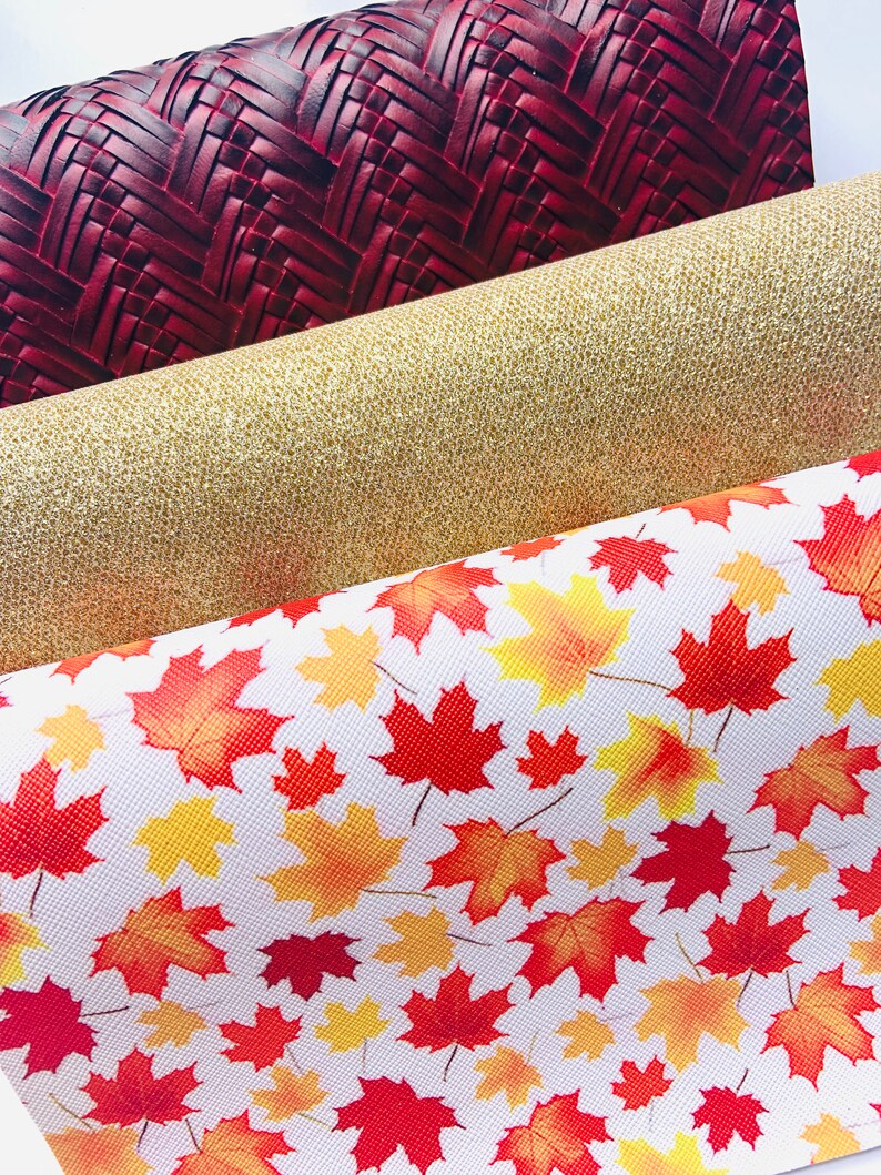 May include: Three fabric swatches with different patterns. The top swatch is a dark red woven fabric. The middle swatch is a gold glitter fabric. The bottom swatch is a white fabric with a red and yellow maple leaf pattern.