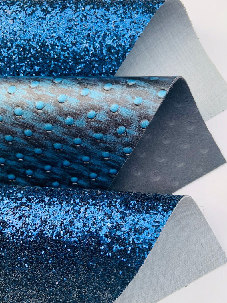 Op de afbeelding: Drie verschillende blauwe stofstalen. De bovenste staal is een glinsterende blauwe stof. De middelste staal is een blauwe stof met een textuurpatroon van kleine cirkels. De onderste staal is een glinsterende blauwe stof.
