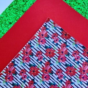 May include: Three sheets of patterned paper. The top sheet is green glitter paper. The middle sheet is red paper. The bottom sheet is white paper with a black and white striped pattern and red poinsettia flowers.