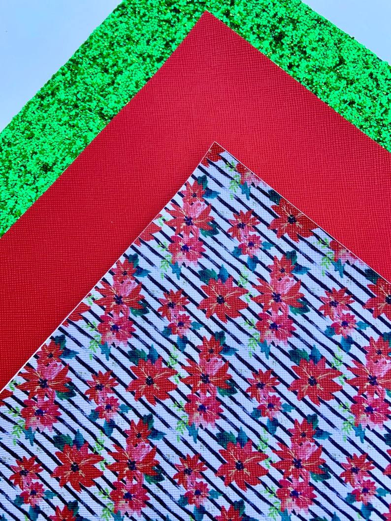 May include: Three sheets of patterned paper. The top sheet is green glitter paper. The middle sheet is red paper. The bottom sheet is white paper with a black and white striped pattern and red poinsettia flowers.