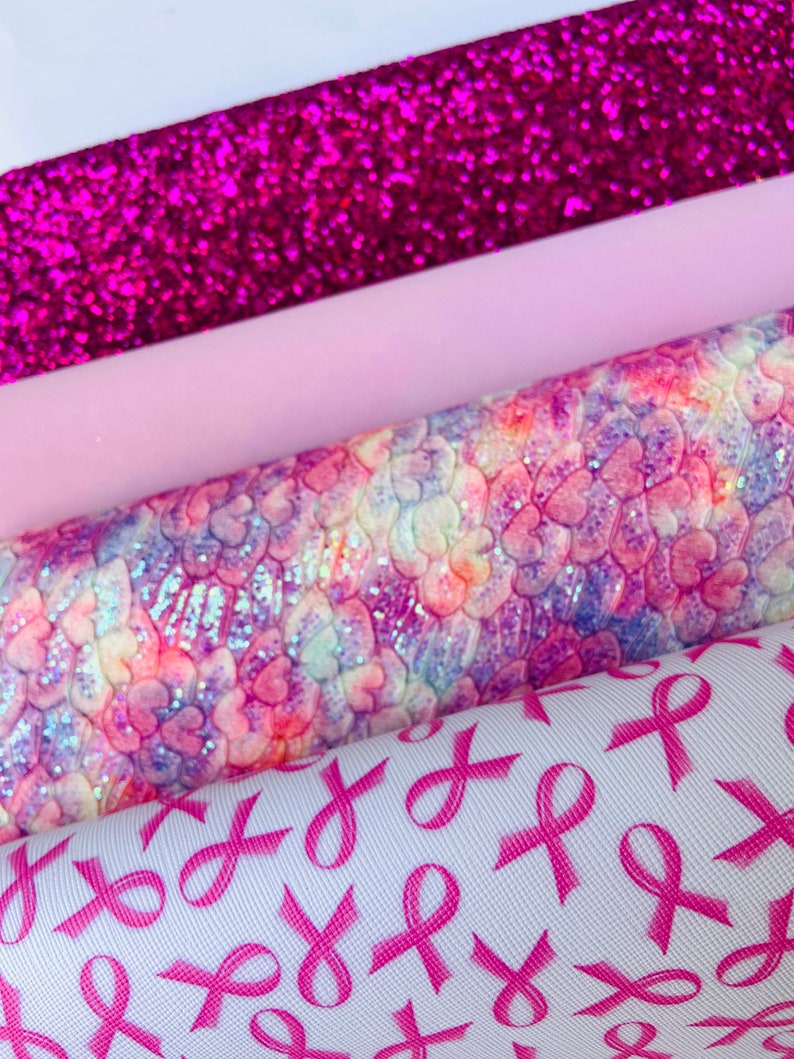 May include: A stack of four different pink patterned fabrics. The top fabric is a sparkly pink glitter fabric. The second fabric is a solid light pink. The third fabric is a pink and white tie-dye fabric with a heart pattern. The bottom fabric is white with a pink ribbon pattern.