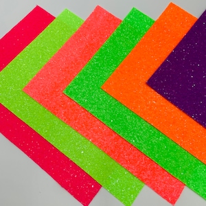 Pu&ograve; includere: Sei fogli di carta glitterata in vari colori, tra cui rosa, arancione, verde e viola. I fogli sono disposti a ventaglio, con il foglio rosa in basso e il foglio viola in alto.