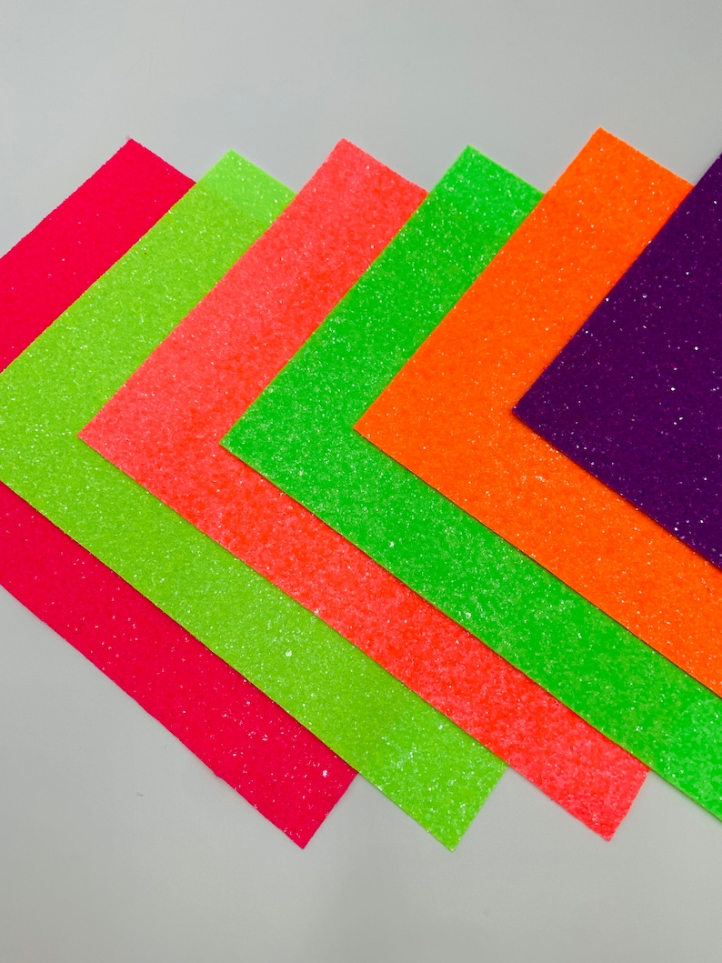 Pu&ograve; includere: Sei fogli di carta glitterata in vari colori, tra cui rosa, arancione, verde e viola. I fogli sono disposti a ventaglio, con il foglio rosa in basso e il foglio viola in alto.
