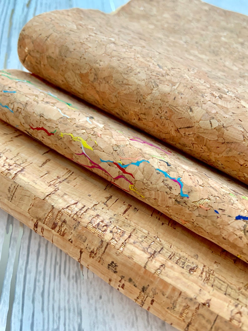May include: Three sheets of cork fabric with different patterns. The top sheet is plain, the middle sheet has colorful lines, and the bottom sheet has a more textured pattern.