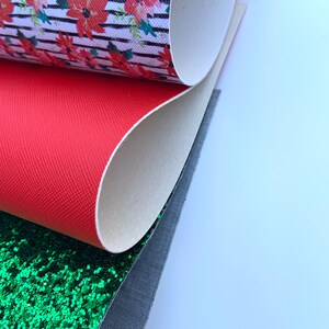 May include: A stack of four different fabric swatches. The top swatch is white with black stripes and a red floral pattern. The second swatch is solid red. The third swatch is green glitter fabric. The bottom swatch is a dark gray fabric.