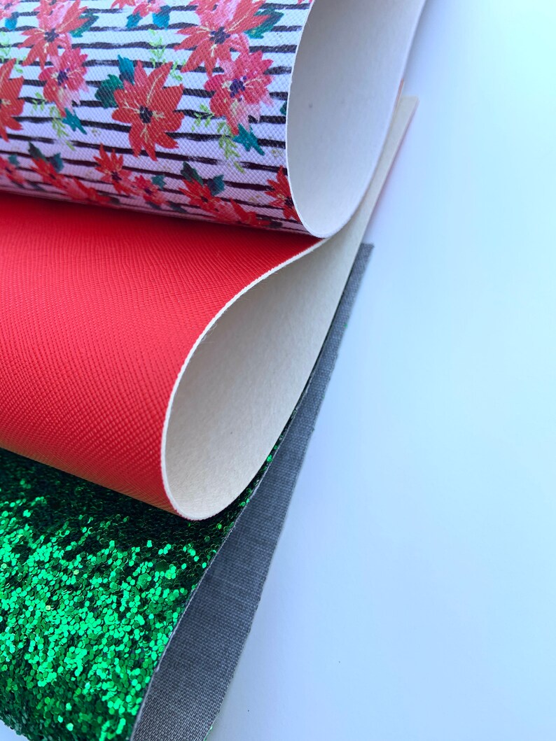 May include: A stack of four different fabric swatches. The top swatch is white with black stripes and a red floral pattern. The second swatch is solid red. The third swatch is green glitter fabric. The bottom swatch is a dark gray fabric.