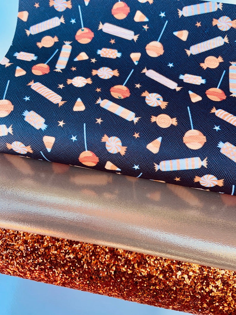 May include: Three fabric swatches: a black fabric with a repeating pattern of orange and white candy, a gold metallic fabric, and a copper glitter fabric.