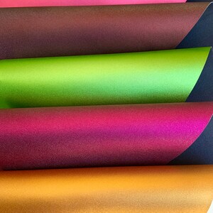 K&ouml;nnte beinhalten: F&uuml;nf Bl&auml;tter irisierendes Papier in verschiedenen Farben, darunter Rot, Braun, Gr&uuml;n, Lila und Gold. Das Papier ist &uuml;bereinander gestapelt, wobei das rote Blatt oben und das goldene Blatt unten liegt.