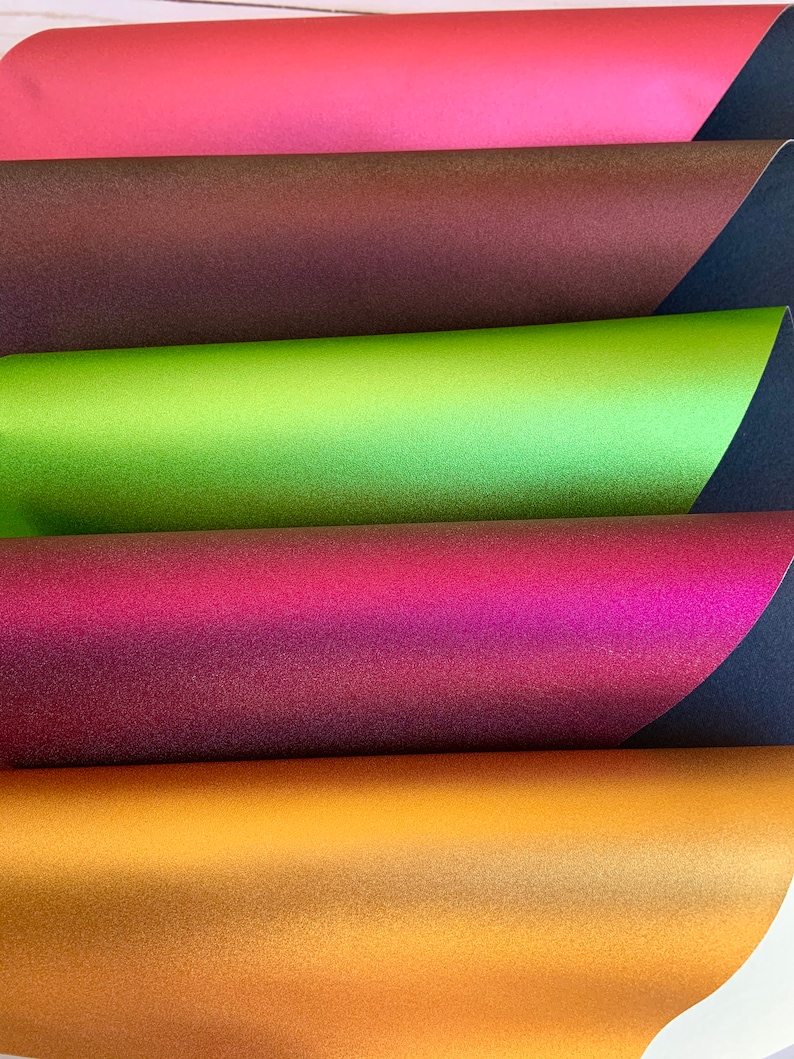 K&ouml;nnte beinhalten: F&uuml;nf Bl&auml;tter irisierendes Papier in verschiedenen Farben, darunter Rot, Braun, Gr&uuml;n, Lila und Gold. Das Papier ist &uuml;bereinander gestapelt, wobei das rote Blatt oben und das goldene Blatt unten liegt.