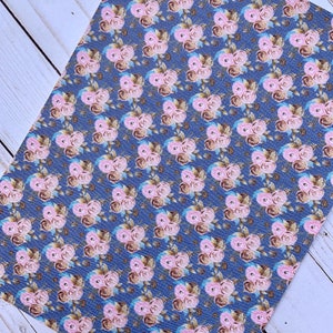 May include: A sheet of floral patterned faux leather. The design features repeating clusters of pink roses with brown and blue accents on a dark blue background. The material has a textured appearance.