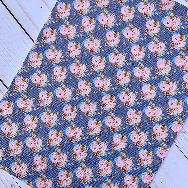 May include: A sheet of floral patterned faux leather. The design features repeating clusters of pink roses with brown and blue accents on a dark blue background. The material has a textured appearance.